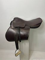 Front angle view displaying the padded seat, knee roll, leather flaps, stirrup leathers, and attached metal stirrups.