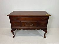 Front angle view of the vintage Lane cedar chest showcasing the carved sunburst motif, brass handles, and cabriole legs.