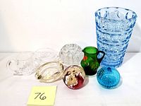 Photo depicting all seven glass pieces in the lot: blue bubble-patterned vase, green floral cream pitcher, red floral paperweight, blue bubble paperweight, clear flower frog, clear ashtray, and oval dish.