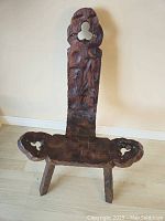 Front view of the antique birthing chair showing carved dark wood, tripod legs, curved seat edges, and backrest with decorative cut-out.