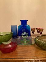 Full lot of vintage colourful glassware includes cobalt blue glass items, green bowls, a green dessert plate with handle, small red figural radish bowl and enamelled cordial glasses