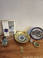 Photo showing the complete lot including the book, multiple decorative plates with Jewish symbolism, and small collectible items on a wooden surface.