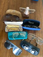 Top-down view of assorted vintage glasses, cases, and a novelty nose stand on a wooden surface