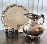 Full view of all items including engraved Chippendale style silver plated tray with scalloped edge, squat silver plated footed water jug with ornate handle, and four cobalt blue glass salt and pepper shakers with lattice design.
