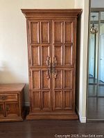 Front view of tall, narrow, four-door solid wood armoire with recessed panels, brass hardware, and carved molding on doors and cornice.