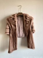 Front view of blonde mink fur capelet showing striped pattern and short sleeves, hanging on hanger.