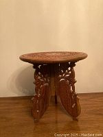 Full view of small round wooden collapsible table showing carved floral legs and round top.