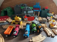 Overview of Brio Thomas the Train set items arranged on table including 4 train engines, track pieces, crane, tunnels, and buildings.