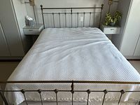 Full view of queen sized bed frame with headboard and footboard, white bedding, showing wrought iron and brass detail. Bed skirt is visible under mattress area.