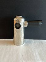 Front and side views of the chrome Freud stove top French press coffee maker showing its cylindrical shape, black handle, perforated side opening, and rounded top.