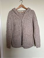 Front view of natural oatmeal Irish knit hooded sweater on hanger showing cable knit pattern and front pockets.