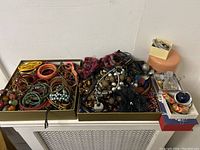 Wide view of all jewelry items showing a massive variety of chunky plastic costume jewelry including necklaces, brooches, earrings, bangles and bracelets spread out in boxes.