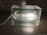 Front view of glass block lamp illuminated showing concave cavity and internal bubbles