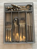 Overview photo of the stainless steel cutlery organized in mesh tray, showing forks, spoons, knives, and ornate iced tea spoons.