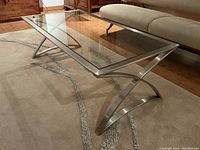Diagonal side view showing the curved aluminum legs and glass surface on a beige rug.