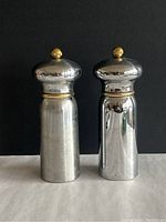 Front view of the pair of silver and brass salt and pepper grinders with reflective silver bodies and brass tops and knobs.