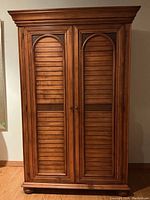 Full front view of armoire showing louvered doors, hardware and crown molding