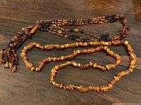 Two vintage amber necklaces displayed on a wood surface; a long single strand and a triple strand with tassels.