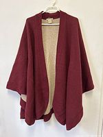 Front view of the maroon wool cape hung on a white hanger showing the open front and draped style.