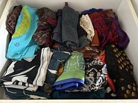 Overview photo showing a drawer filled with neatly folded women's scarves with various patterns and colors including turquoise, black, brown, purple, and green.