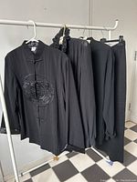 Three black vintage mandarin collar tops and one black skirt hanging on a rack, showing overall lot contents