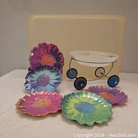 Five colorful Andy Warhol melamine flower-shaped plates, glass fruit bowl on wheels, pale yellow lucite tray in background
