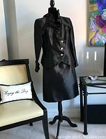 Full view of the black two-piece cocktail outfit on mannequin showing the blazer with ruffled collar and matching skirt.