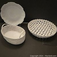 Three white ceramic serving pieces on black surface: oval handled basket, round woven basket, and large platter