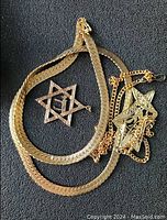 Four pieces of gold-tone costume jewelry on black background including chain necklace and three pendants with Star of David shapes.