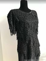 Front side profile view of black lace dress with detailed lace top and pleated skirt showing texture and length.