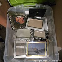 Large bin containing multiple silver coloured picture frames in various sizes and styles including ornate and simple frames.