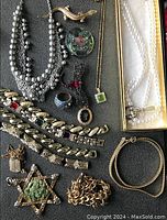 Assorted costume jewelry including necklaces, bracelets, brooches, and rings arranged on grey fabric.