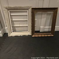 Two ornate wooden frames side by side against a wall, one white and one dark brown.