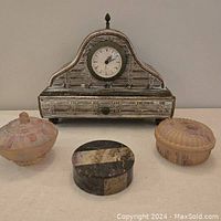 Four items on a flat surface: a vintage decorative dresser clock and three trinket boxes composed of two satin glass and one marble.