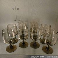 Photo showing all 8 smokey amber footed wine glasses grouped together on a flat surface with textured wall background.