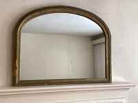 Full view of the antique arched mirror with a carved wood frame in antique gold finish.