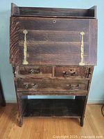 Full front view of the antique mission style desk showing fold down front with brass hinges, three drawers, and bottom shelf
