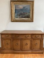 Front view of oak Krug sideboard buffet, showing four drawers on top and four cabinet doors below, metal hardware, medium brown oak finish. Wall painting and hardwood floor visible.
