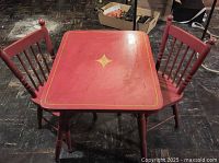 Front view showing vintage red painted child-size square kitchen table with gold detailing, with two matching chairs positioned on either side.