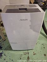 Front view of white NOMA dehumidifier on worn basement floor, showing minimal wear.