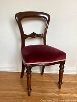 Side view of antique balloon back dining chair showcasing carved wooden frame and red velvet upholstered seat.
