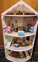 Full front view of the three-level KidKraft Chelsea Doll Cottage corner dollhouse with detailed painted room backgrounds and an assortment of furniture in each room.