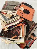 Several stacks of assorted 45 RPM vinyl records with paper and cardboard sleeves in varying conditions.