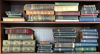 Shelf with 28 antique Bibles and religious books of varying sizes and bindings including heavily worn leather covers and cloth covers in dark and muted tones, some tied with string.
