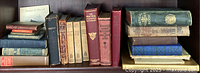 Wide shot of multiple stacks of antique books including poetry and dictionaries with leather and cloth covers showing wear and age.