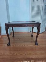 Front wide view of mahogany Chippendale style end table showing carved legs and ball claw feet on hardwood floor.
