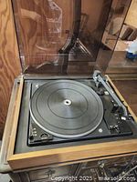 Front close-up of the Noresco Dual Compact stereo turntable showing the platter, tonearm and base housed in wooden cabinet with raised clear plastic dust cover.
