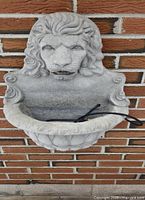 Front view of the plaster lion wall fountain installed on brick wall.