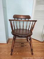 Front angle view of solid wood round seat captain's chair with turned spindles and nail heads on seat.