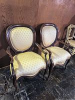Pair of vintage curved armchairs with cream patterned upholstery, solid wood frames, and carved details on backrest tops.